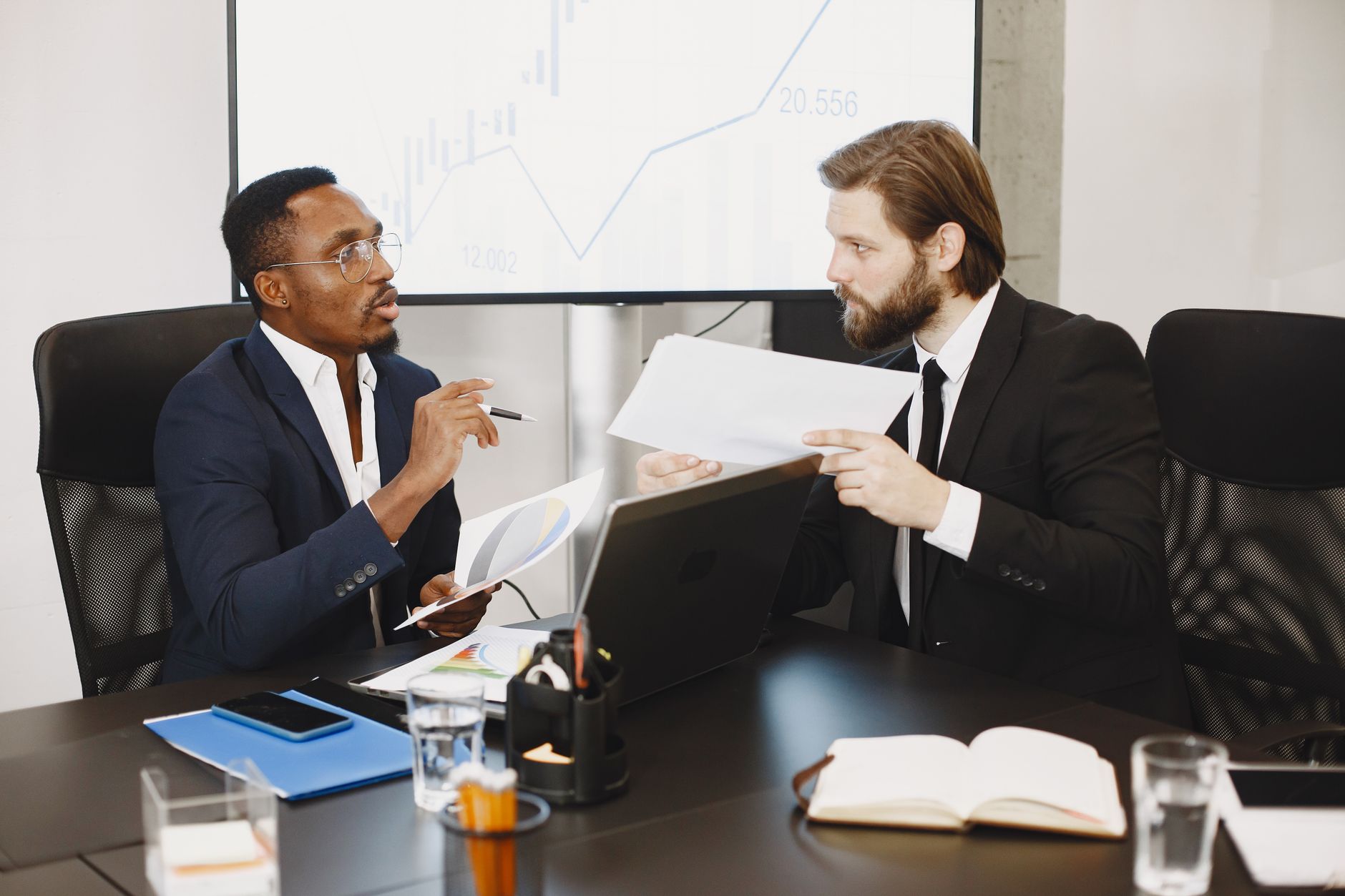Two business professionals engaged in a planning meeting, discussing documents in a modern office setting. — Eco-Friendly Sur