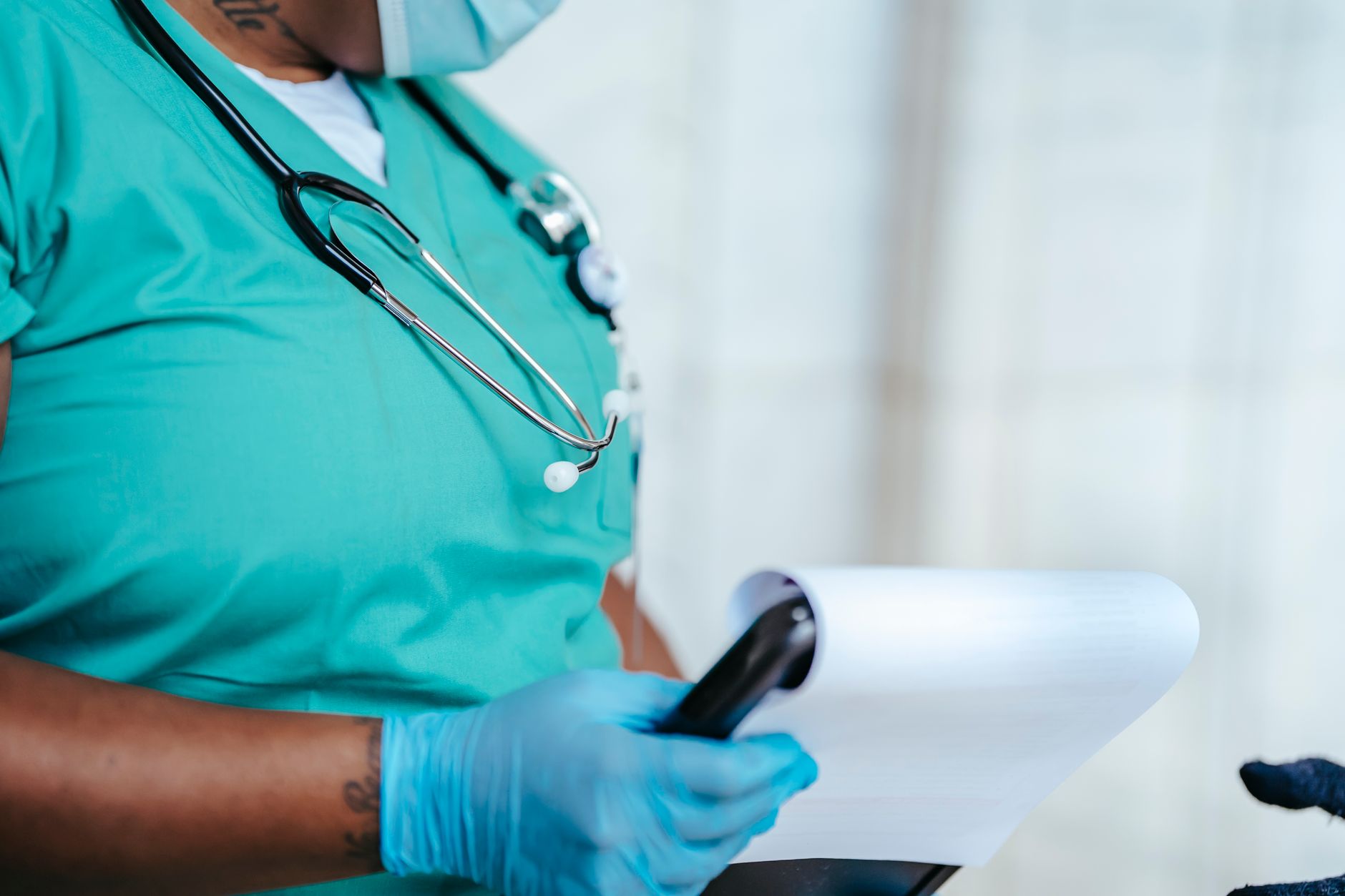 Side view of crop anonymous tattooed ethnic female medic in uniform with stethoscope and papers on clipboard — Elevating Stan