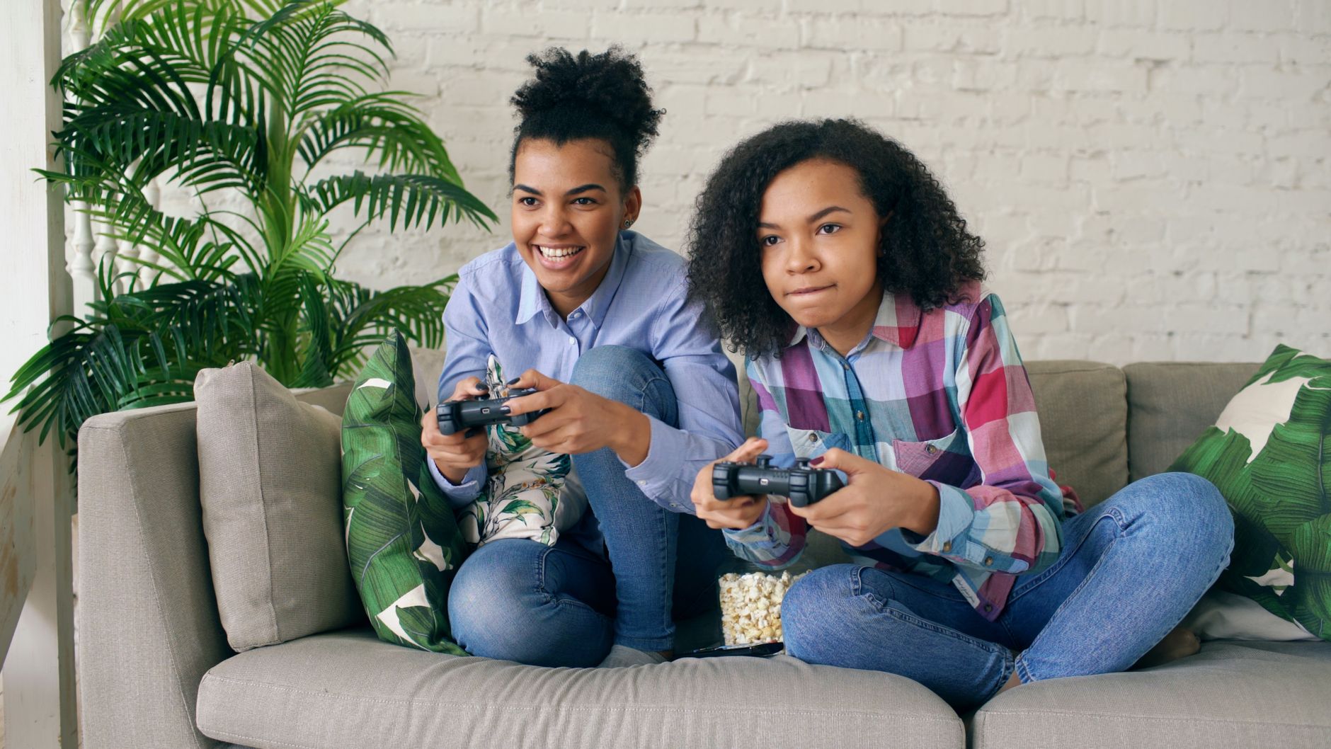 Two teenagers playing video games together on a comfortable couch, surrounded by indoor plants. — Find the Official Bet365 Ko