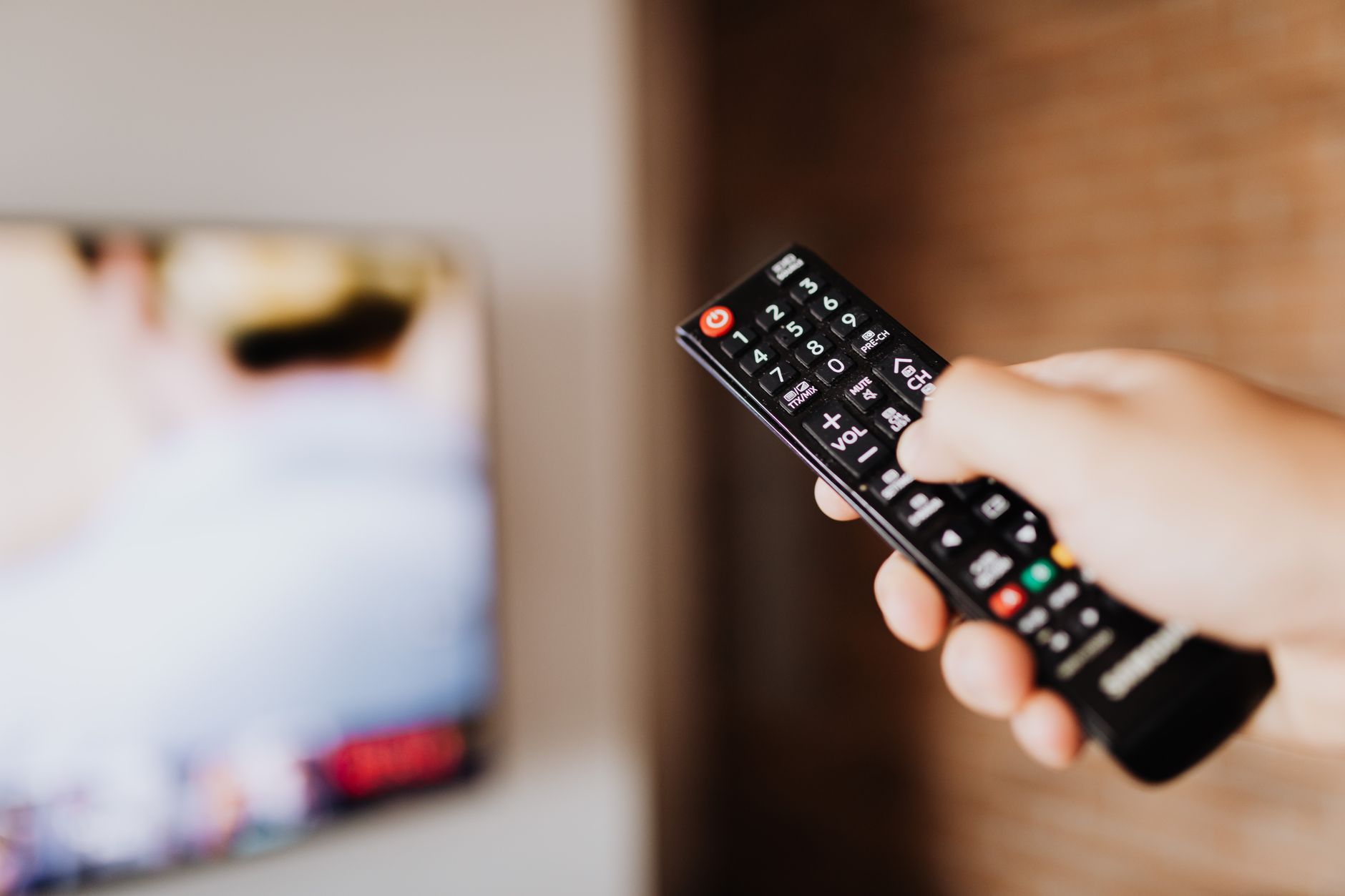 Close-up of a person using a TV remote with a blurred background indoors. — Free Sports Broadcast Site That Brings You to the