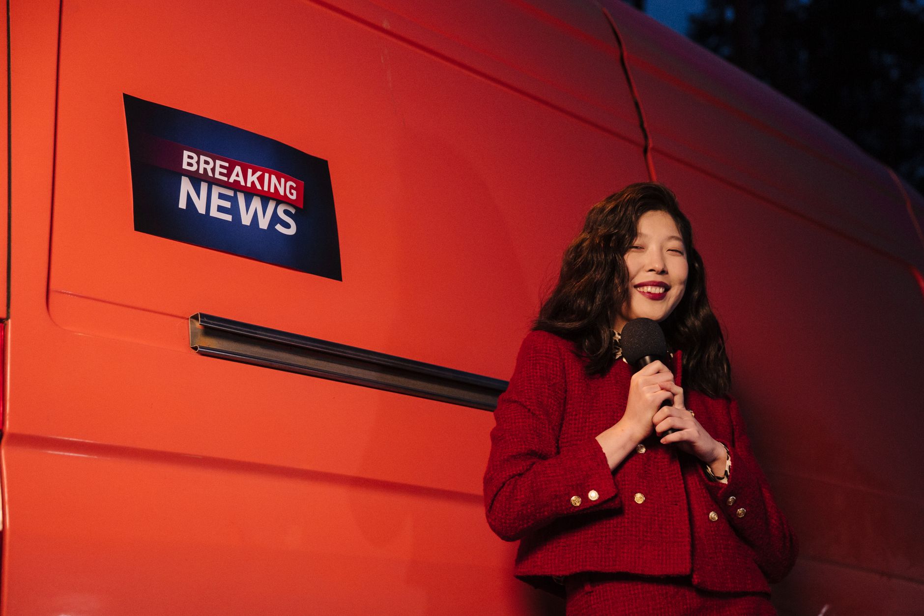 Asian female reporter smiling with microphone besides a news van at night. — Novi Branch Office of Homewatch CareGivers - Nov