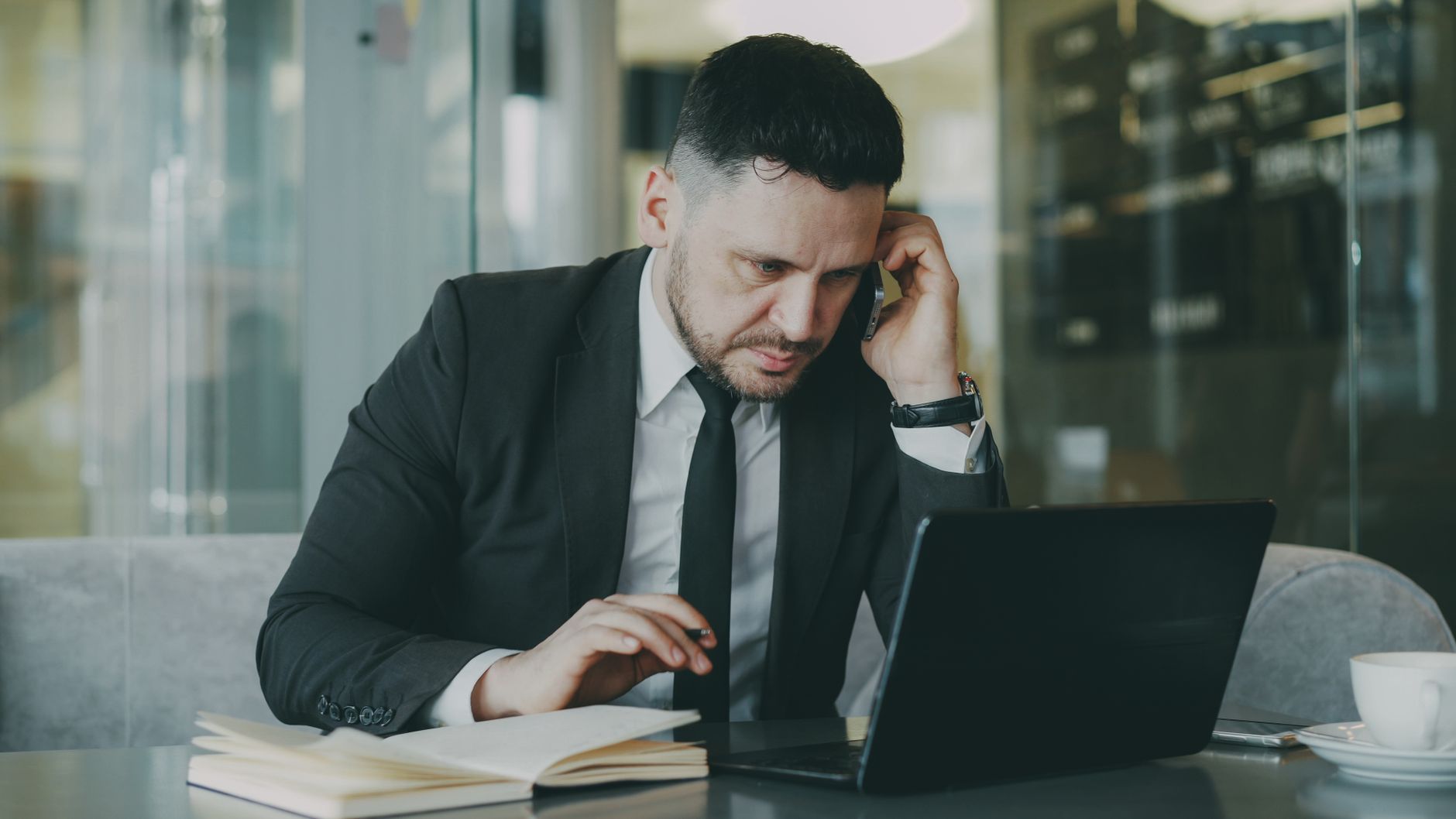 Focused businessman in suit multitasking on phone and laptop in modern office. — Saving Lives Through Innovation: Dr. Zachary