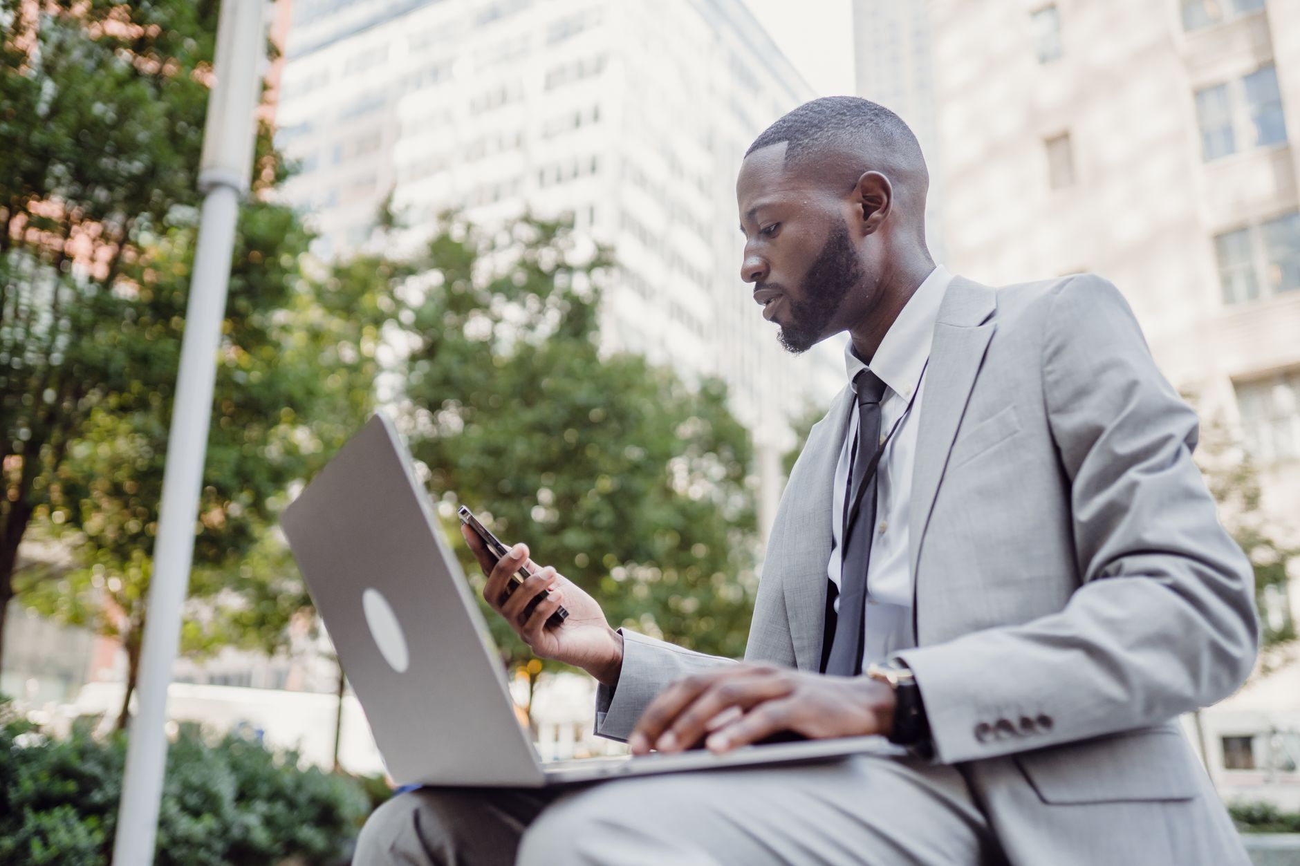 Businessman in a suit using a laptop and smartphone in an urban setting, blending technology with business. — Strategic Leade