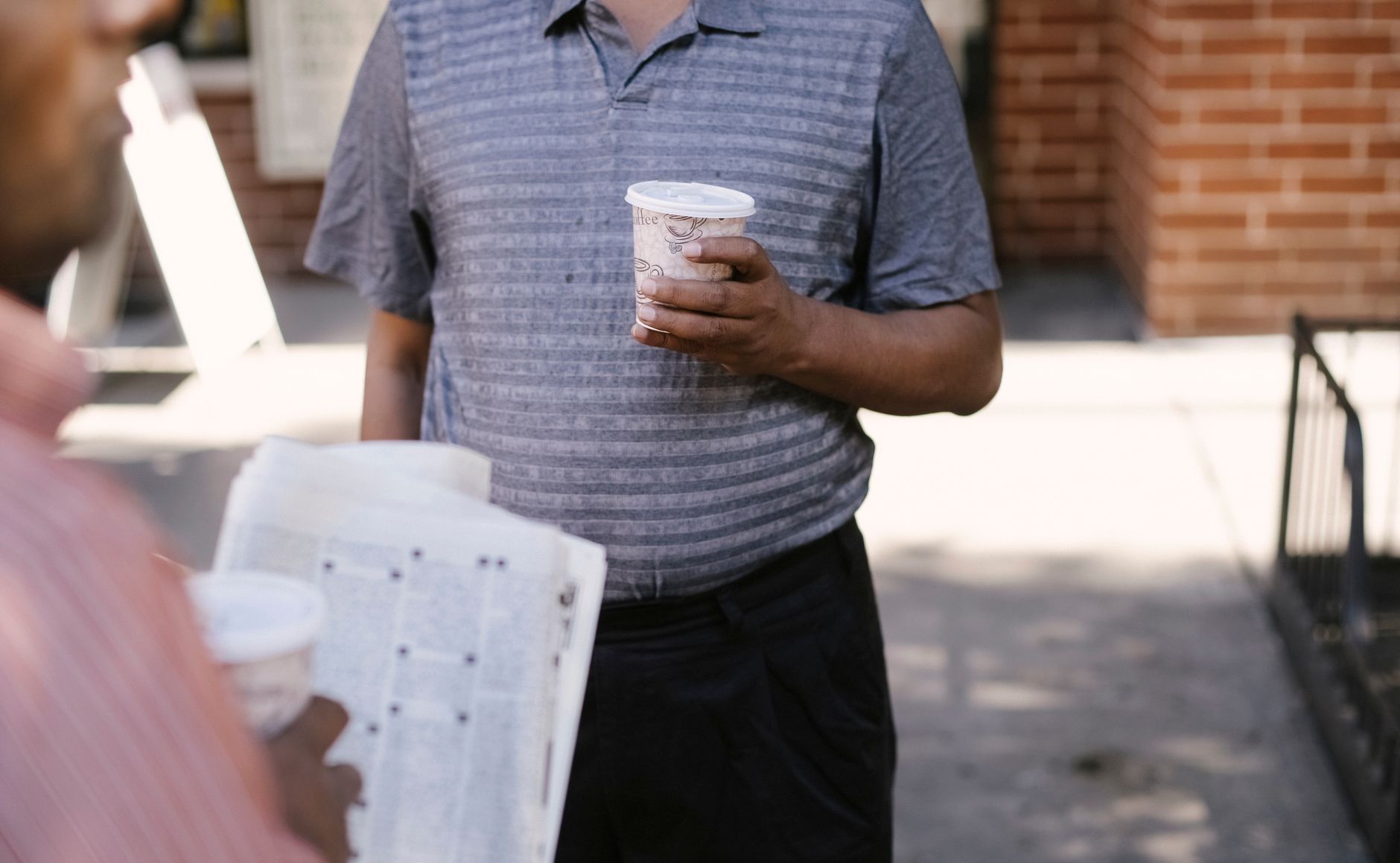 Crop anonymous ethnic male friends with coffee to go and newspaper speaking on city pavement — Understanding the UK Steroid M