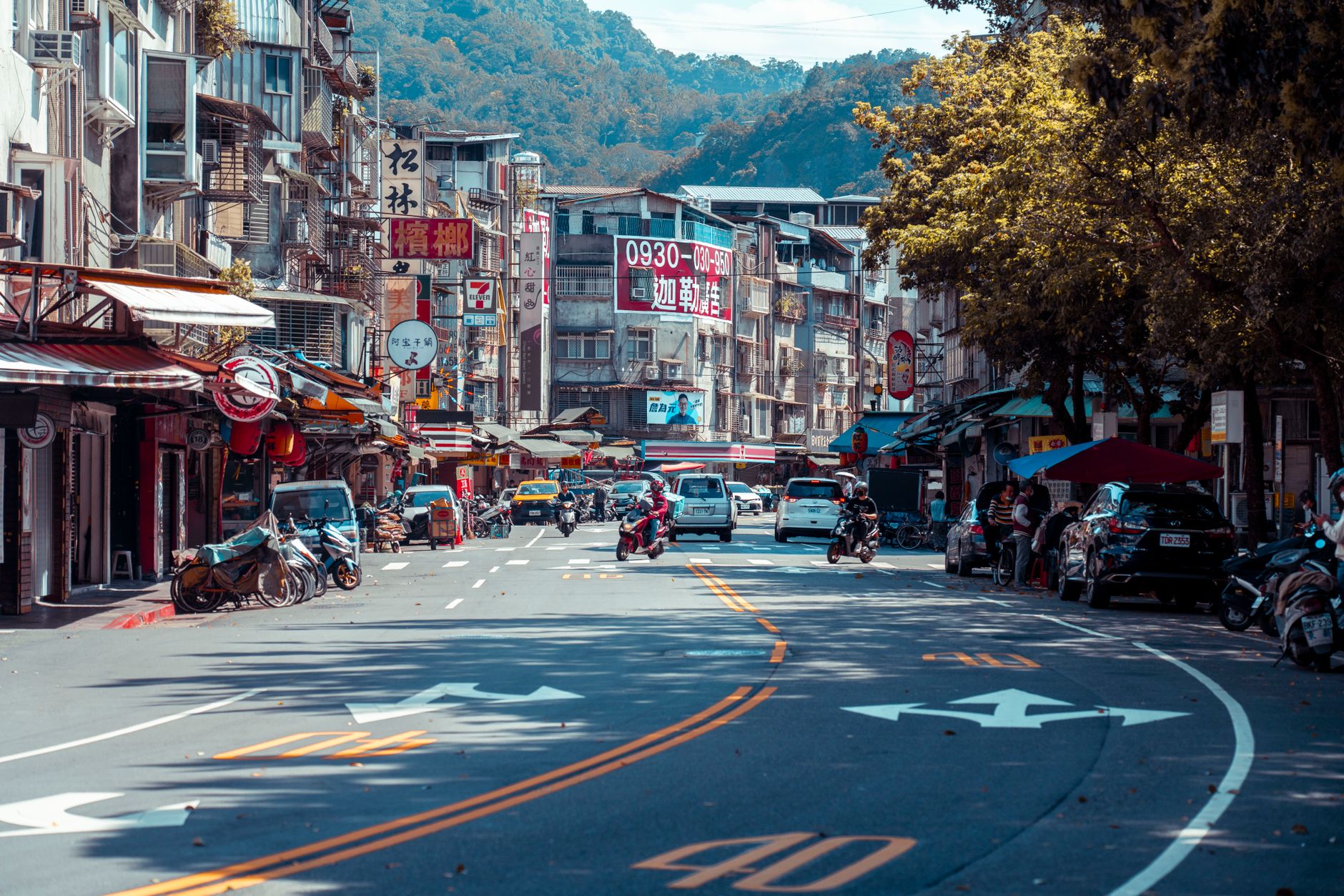 Vibrant urban street scene with shops, vehicles, and mountains in an Asian city. — Unveiling Tomorrow: Stuart Piltch Explores