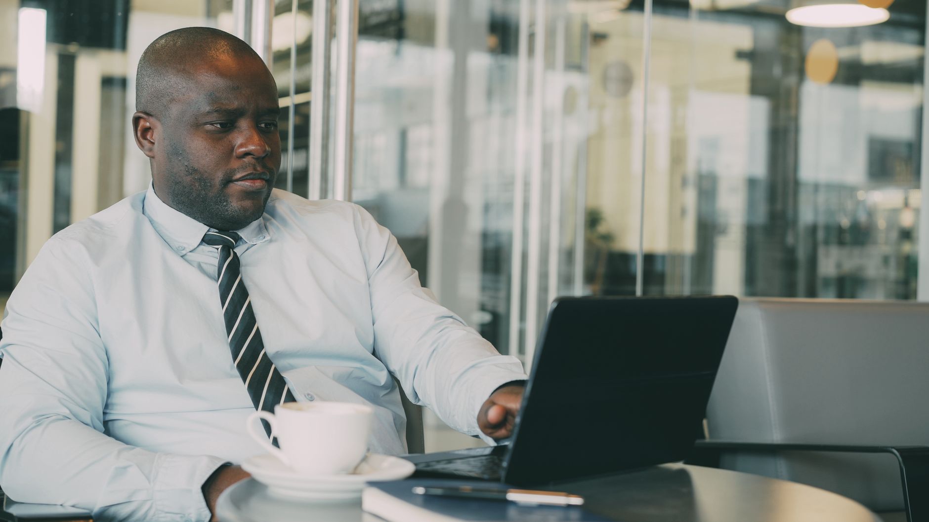 Focused businessman uses laptop in stylish cafe, sipping coffee. Perfect for business or lifestyle themes. — Where to Find In